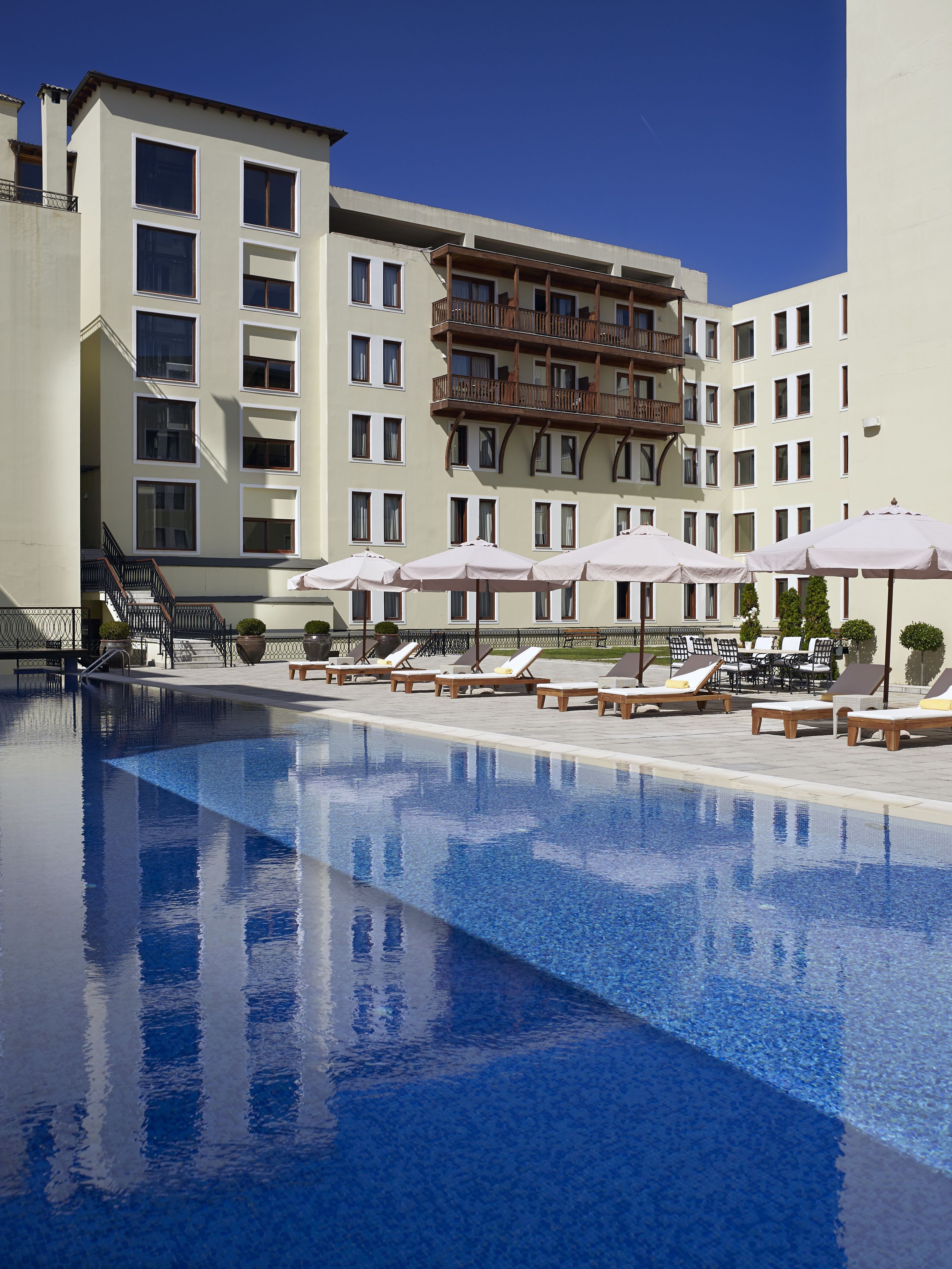 A swimming pool with lounge chairs and umbrellas, surrounded by a multi-story building with balconies.