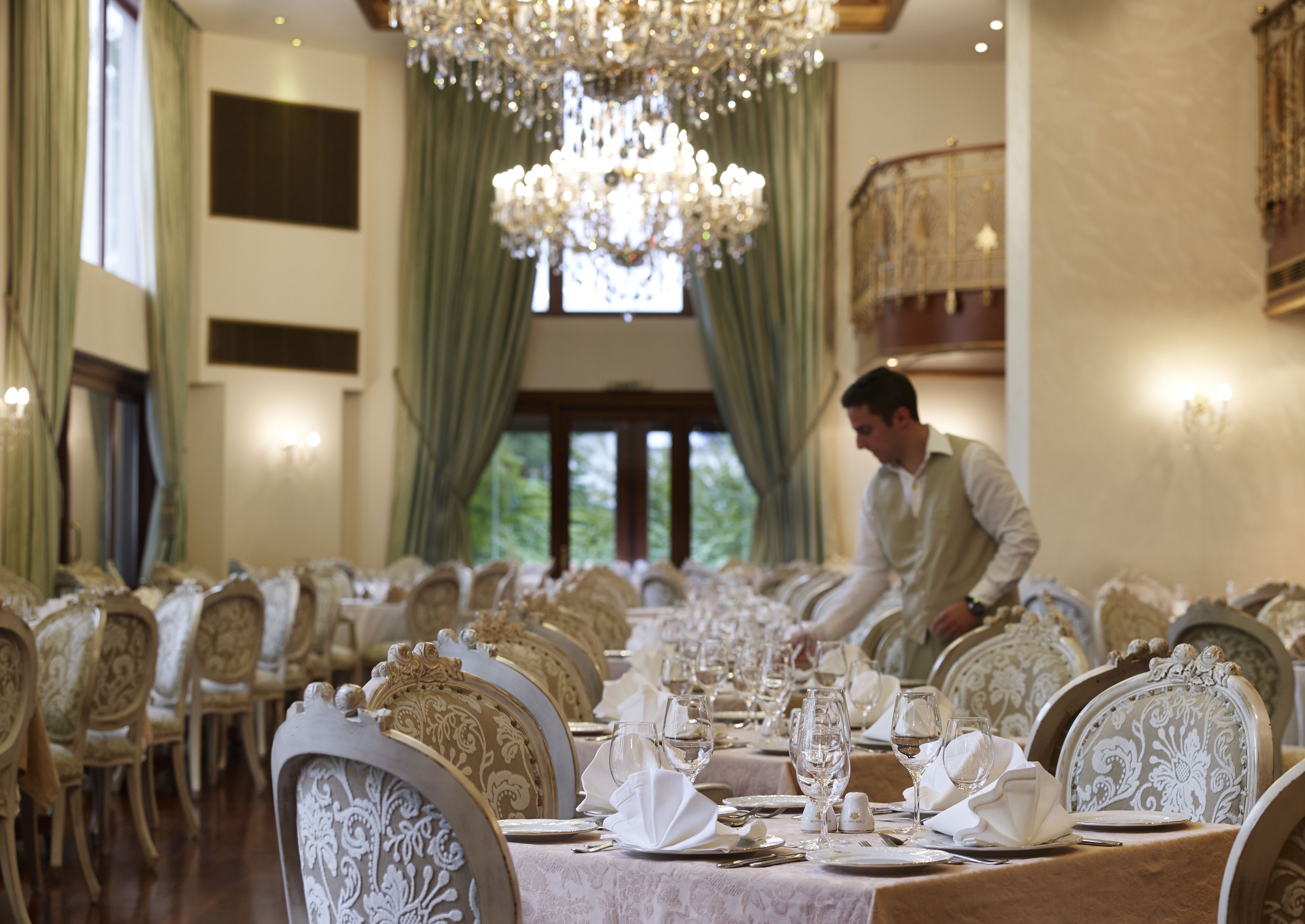 Une salle à manger élégante, avec des chaises richement décorées, une longue table dressée pour un repas et un lustre.