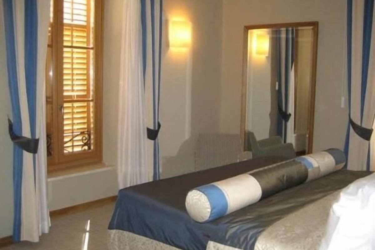 A hotel room with a bed, curtains, a window with blinds, and a mirror.