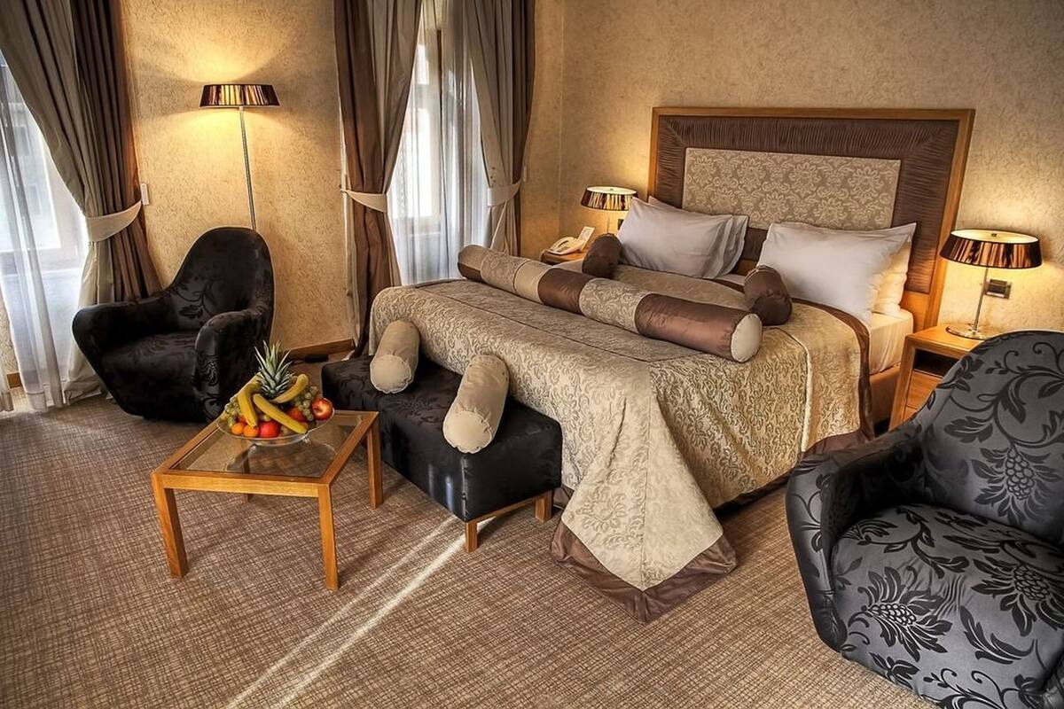 A hotel room with a large bed, two bedside tables, a chair, and a small table with fruit.