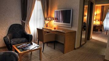 A hotel room with a desk, a chair, a TV, and a small table with magazines.