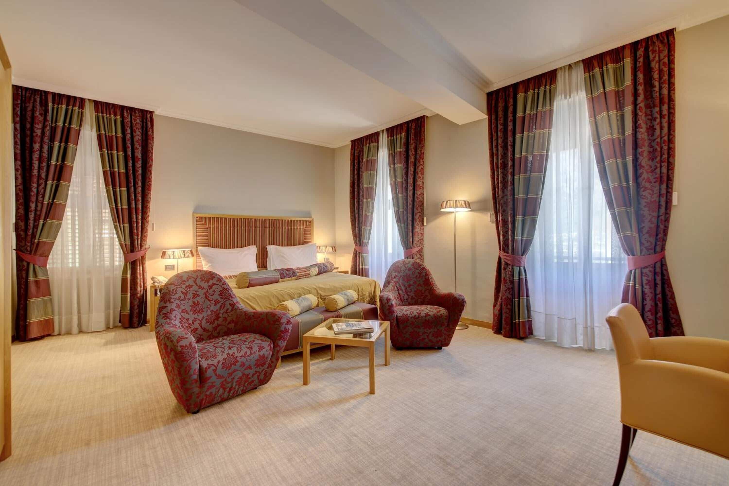 Una habitación de hotel con una cama, dos sillones, una mesa de centro y una lámpara.