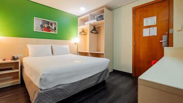 A hotel room with a bed, a nightstand, a wardrobe, and a green wall.