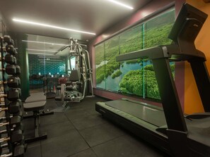 Un gimnasio con cinta de correr, máquinas de pesas y un amplio ventanal con vistas a la naturaleza.