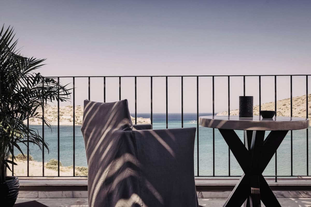 A balcony with a view of the sea, a round table with a candle, and a potted plant.