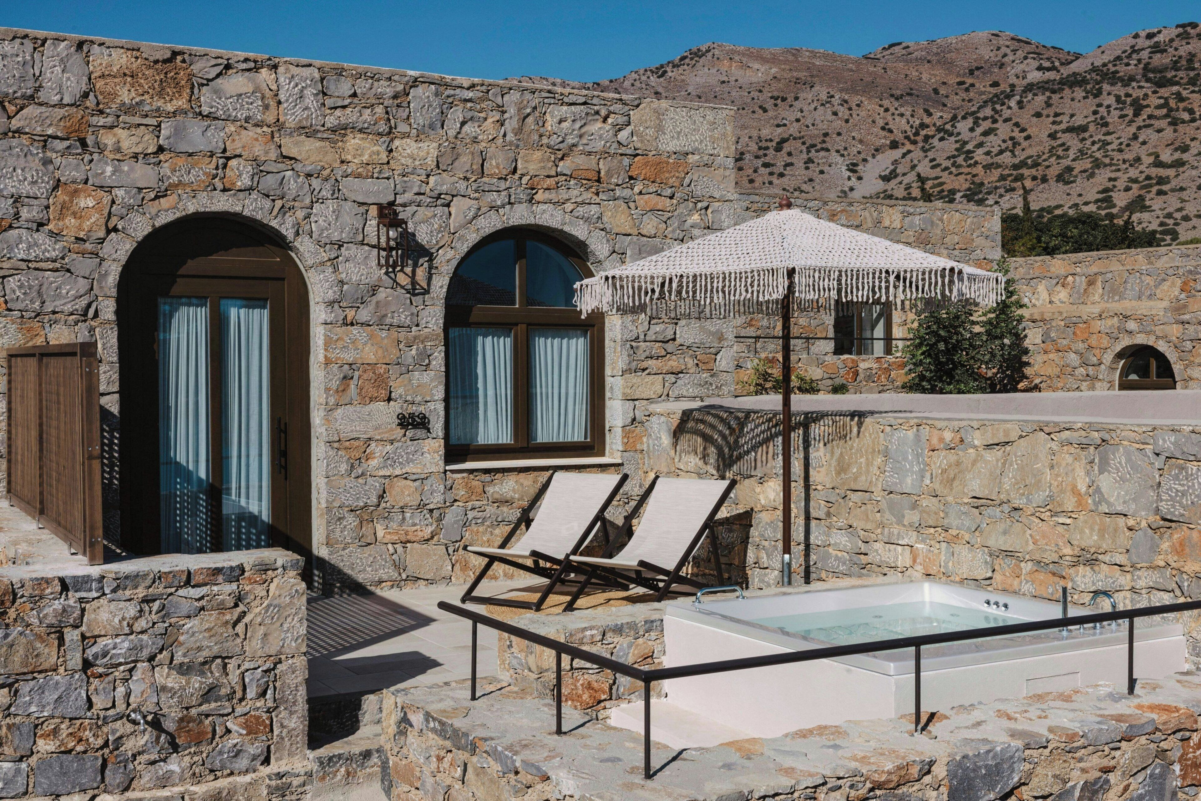 Un edificio de piedra con dos ventanas arqueadas, una piscina y sillones de descanso.