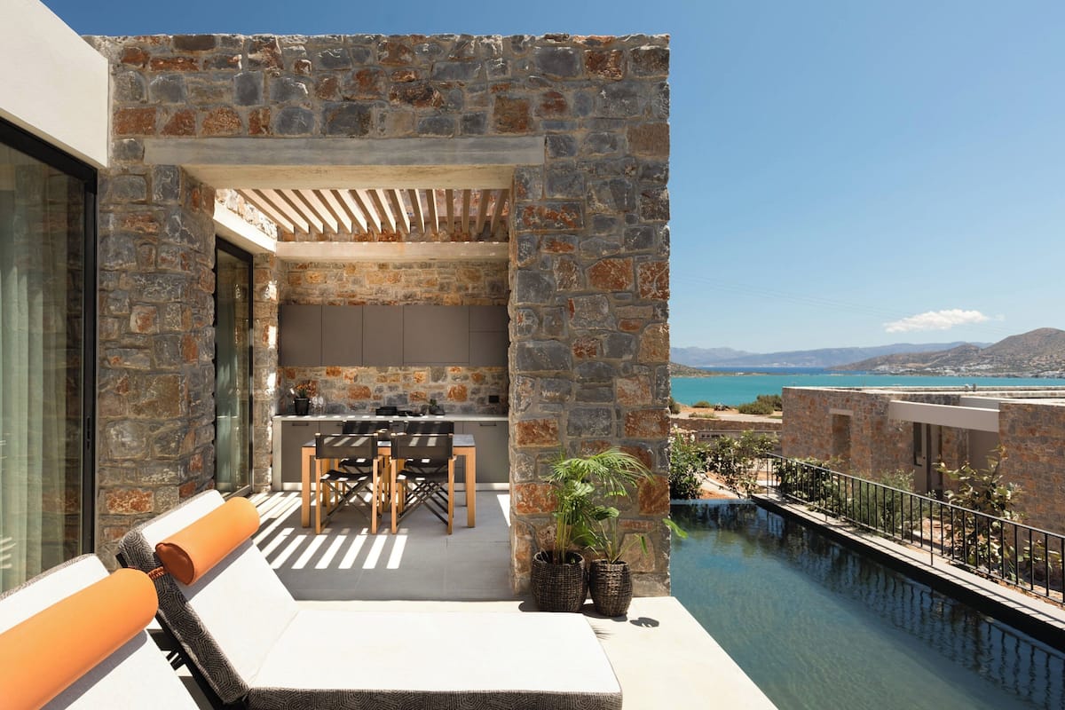 A balcony with a stone wall, a dining area with chairs and a table, and a view of the sea.
