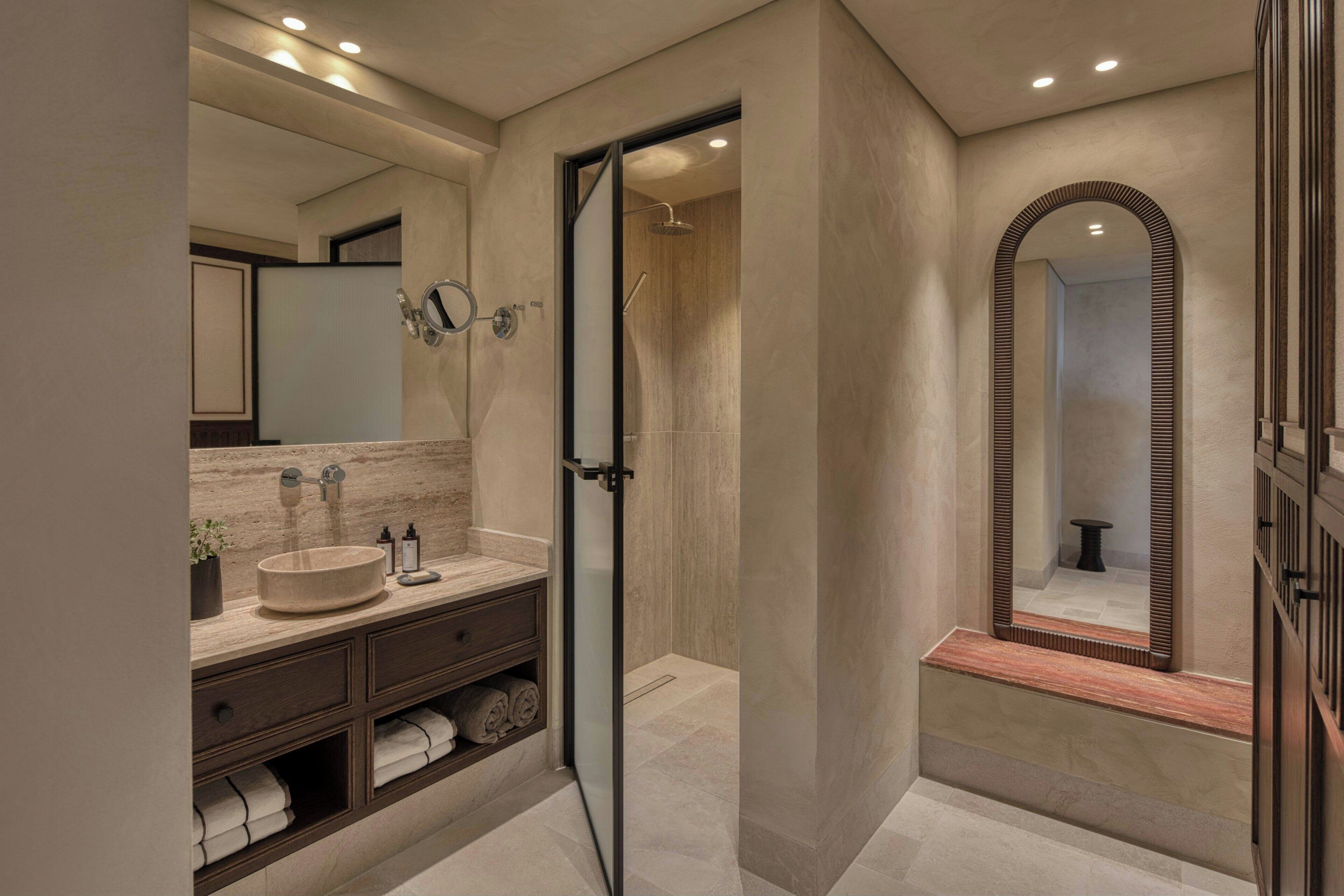 A modern bathroom with a large mirror, a round sink, and a glass-enclosed shower.