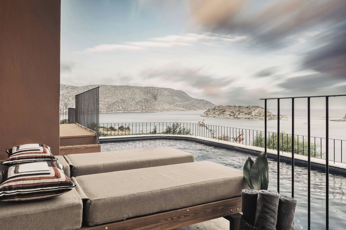 A poolside area with lounge chairs and a view of a lake and mountains.