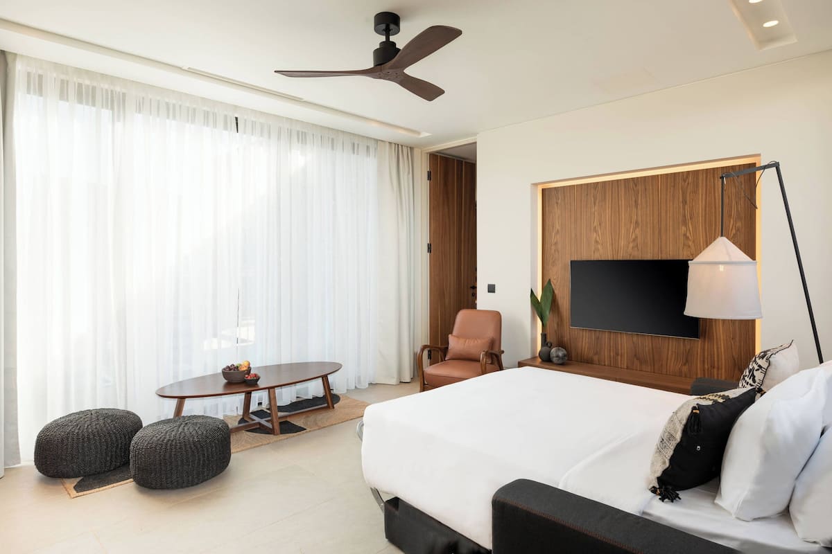 A modern hotel room with a large bed, a desk, a chair, and a TV mounted on the wall.