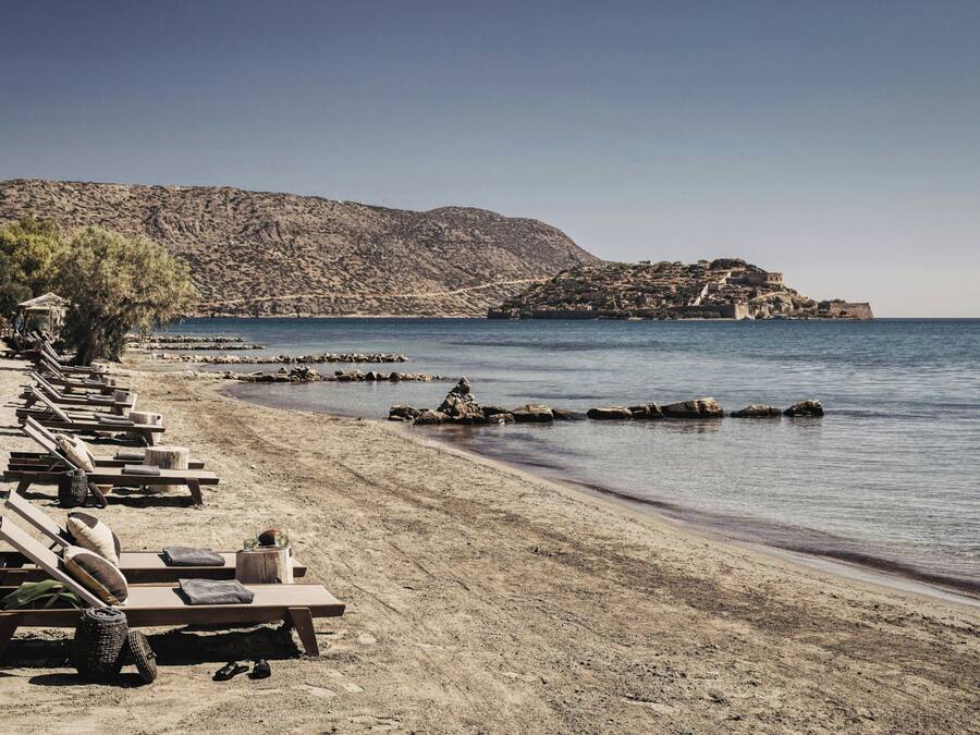 Una playa con tumbonas y una colina rocosa al fondo.