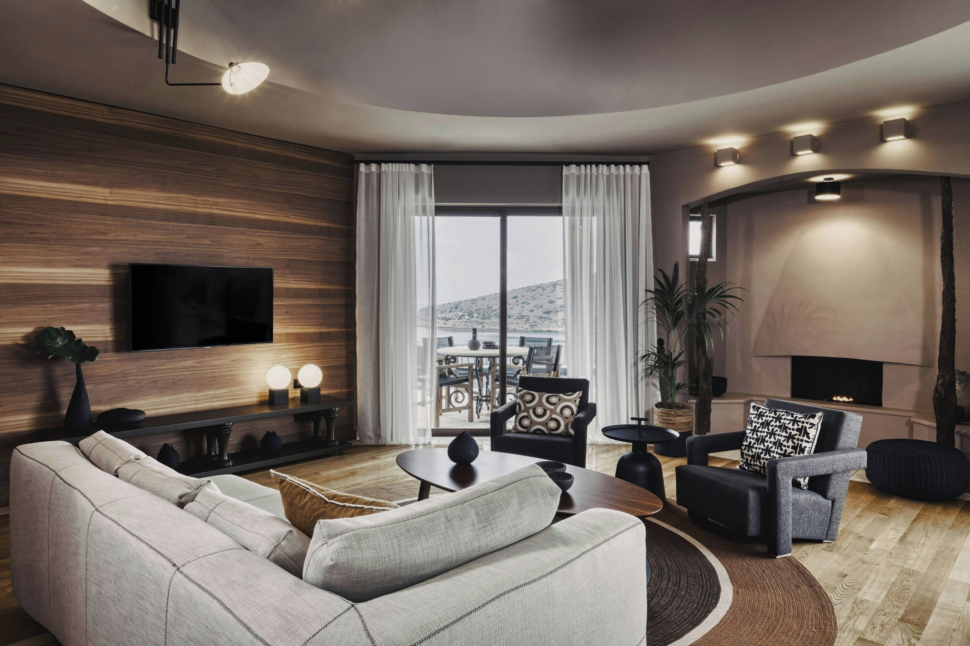 A modern living room with a sofa, armchairs, a TV, and a fireplace.