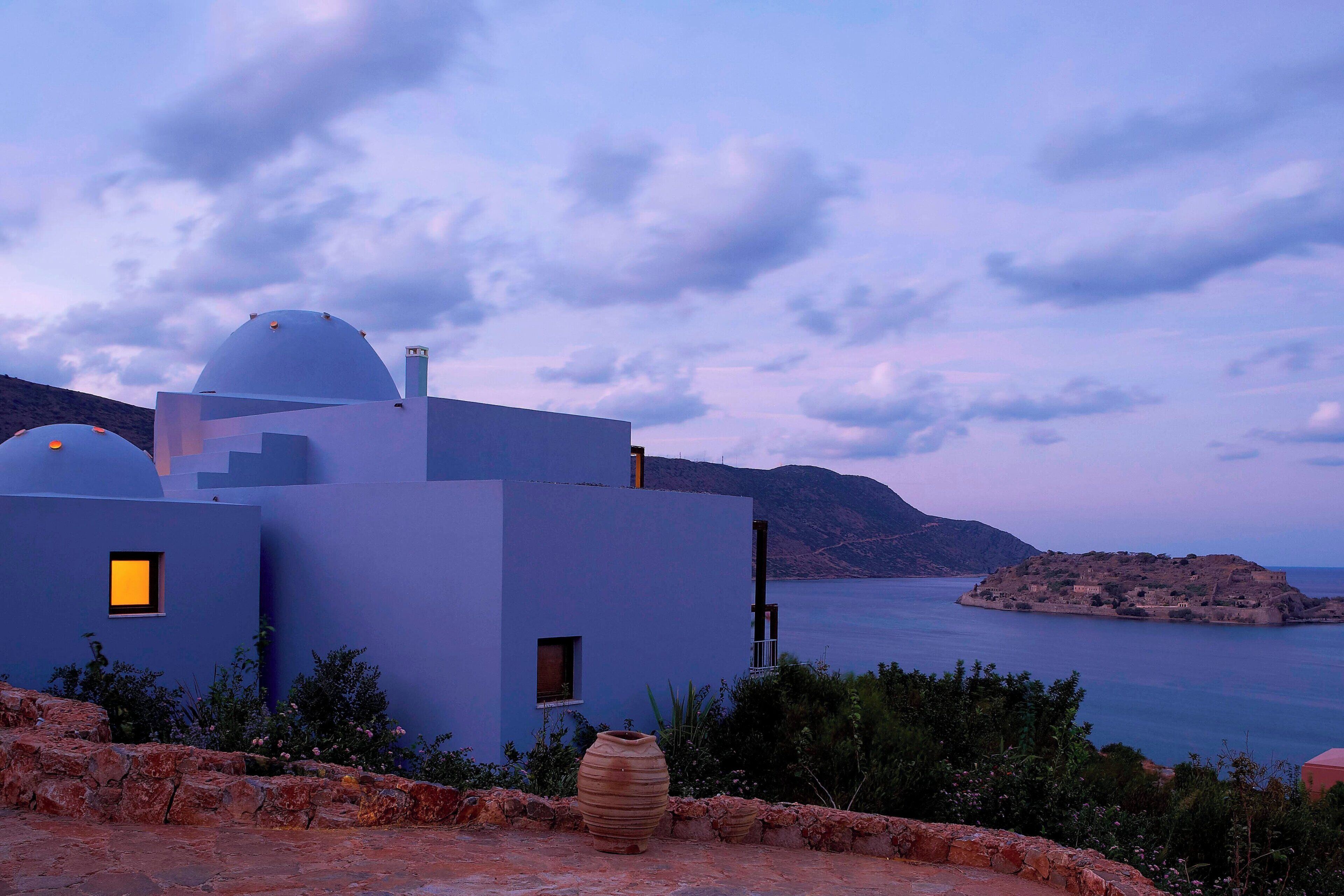 A modern building with a dome and a small window, overlooking a body of water and a distant island.