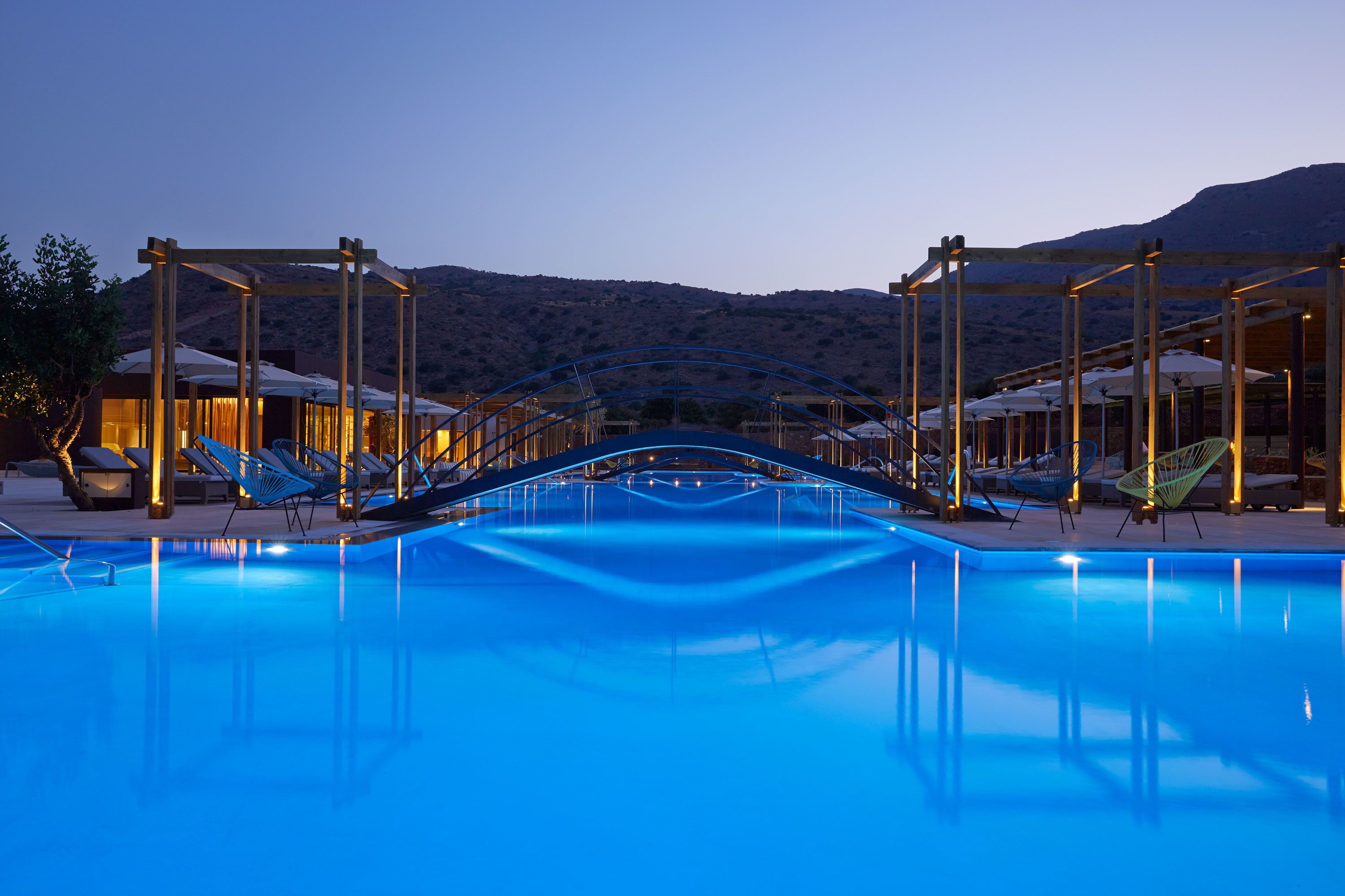 A swimming pool with a wooden deck and lounge chairs, surrounded by a mountainous landscape.