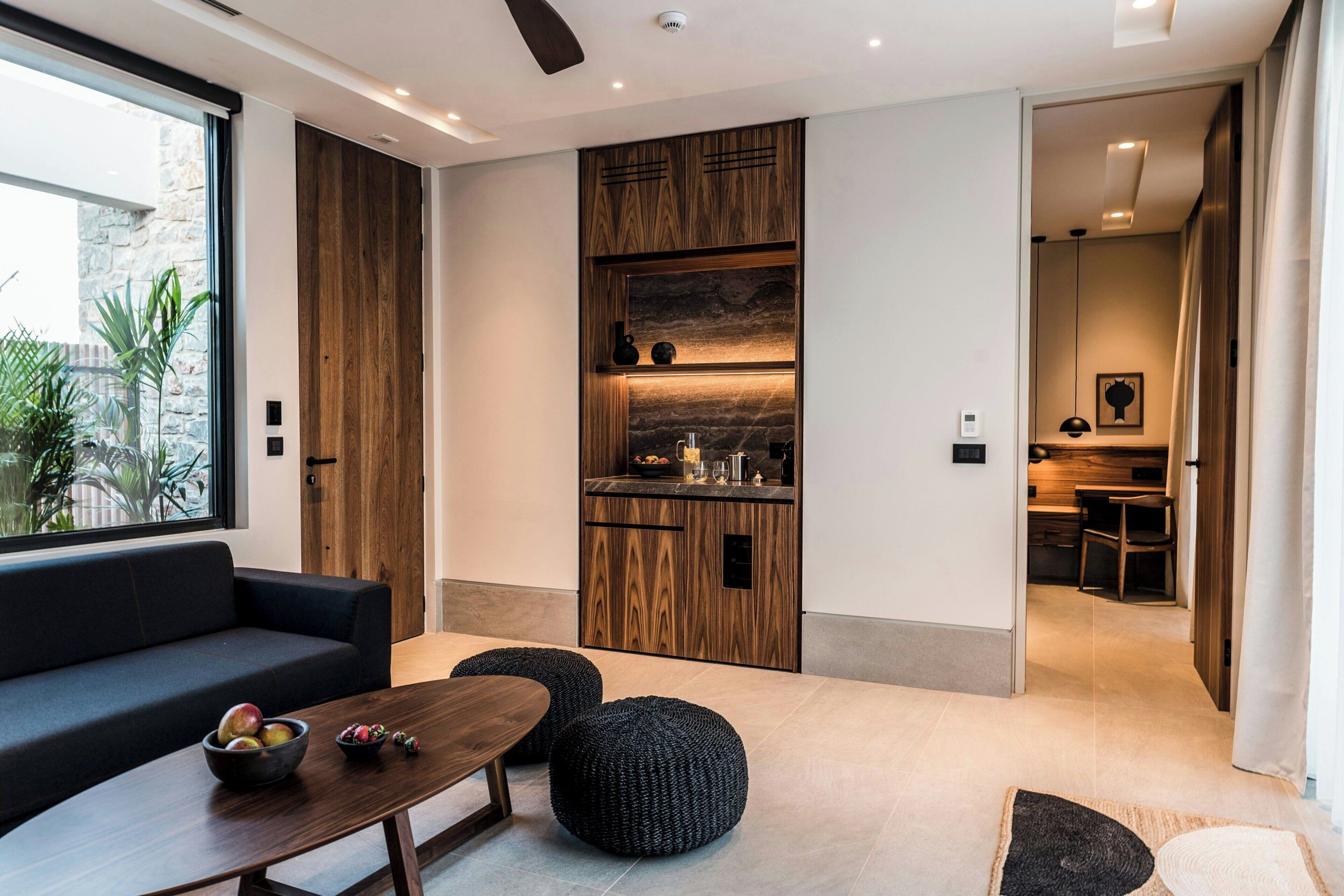 Una sala moderna con sofá, mesa de centro y otomanas, una cocina con armarios de madera y un comedor con mesa y sillas.
