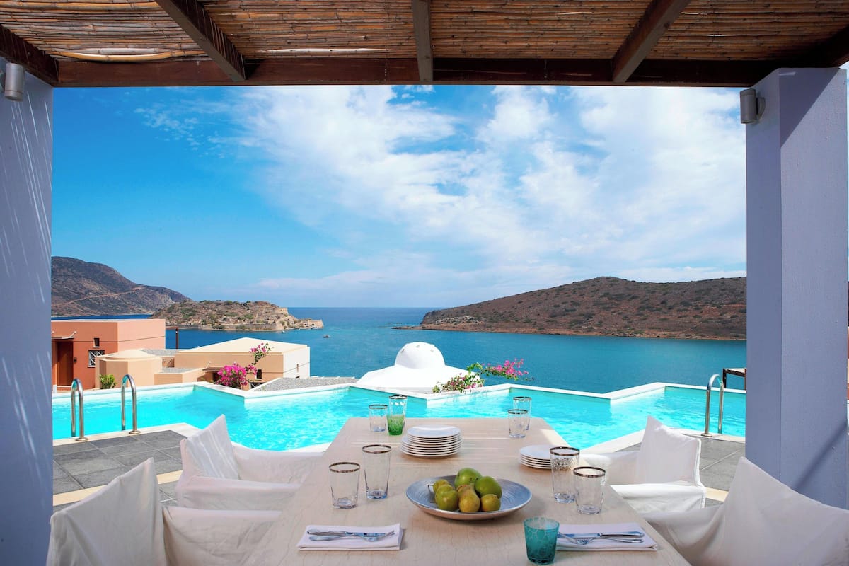 A table set for dining with a view of a swimming pool and the sea.