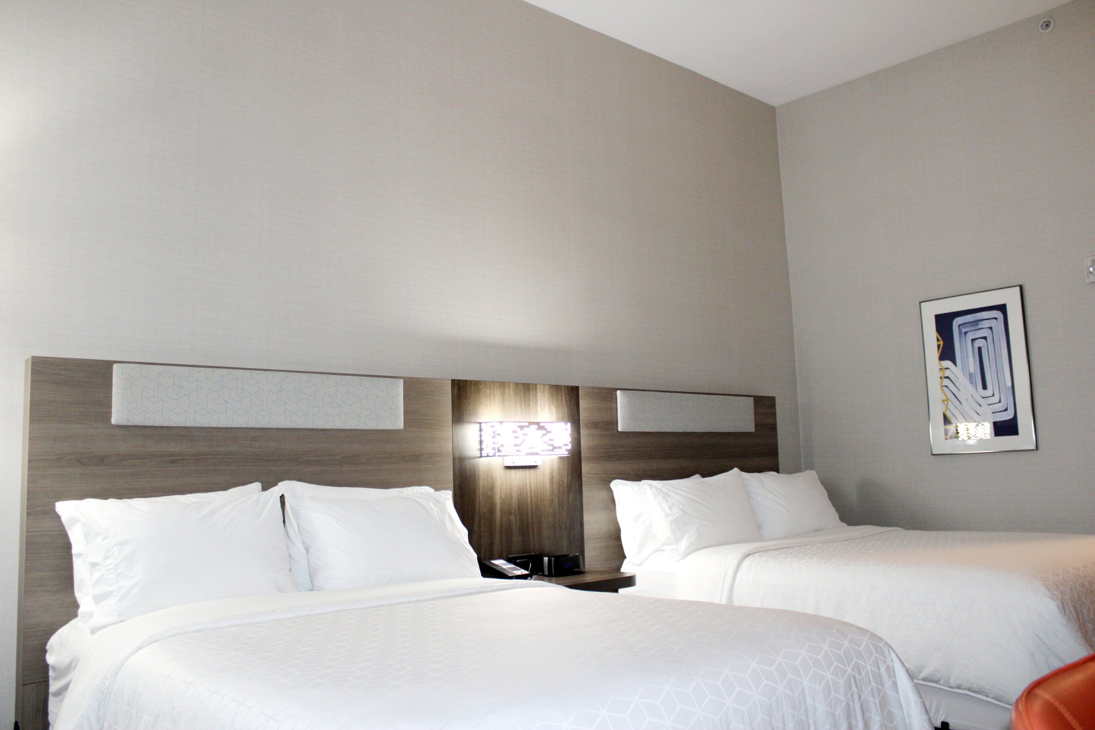 A hotel room with two beds, a wooden headboard, a nightstand, and a wall-mounted light fixture.