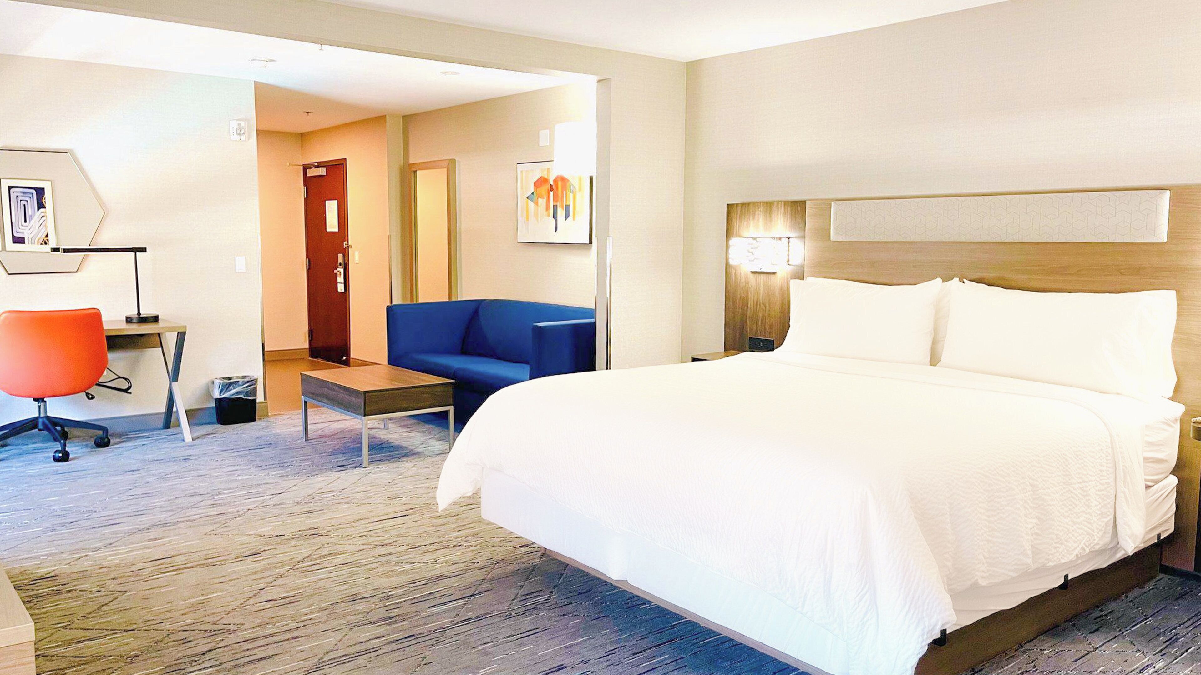 A hotel room with a large bed, a desk with a chair, a blue sofa, and a small table.