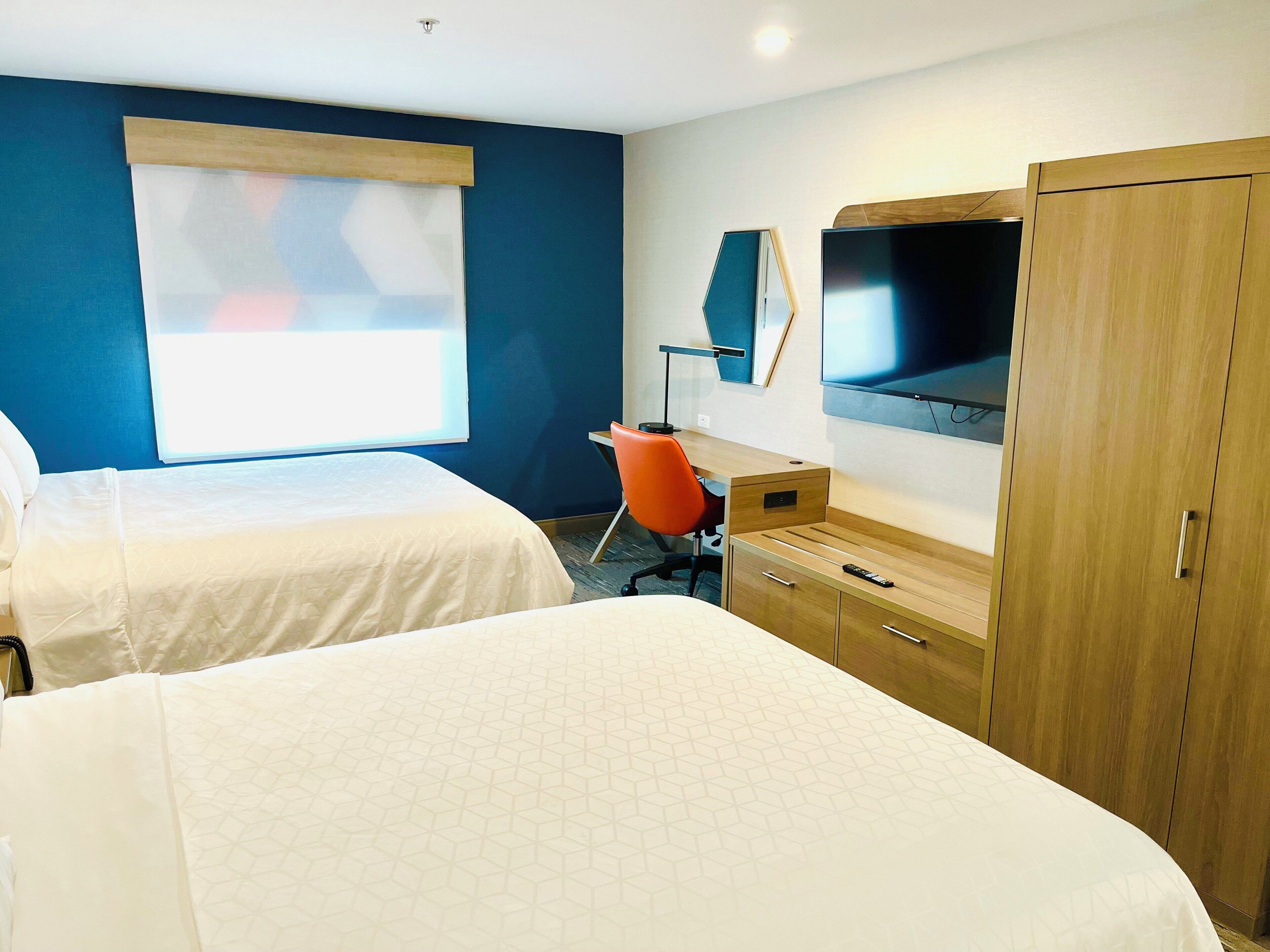 Une chambre d’hôtel avec deux lits, un bureau, une télévision et une armoire.