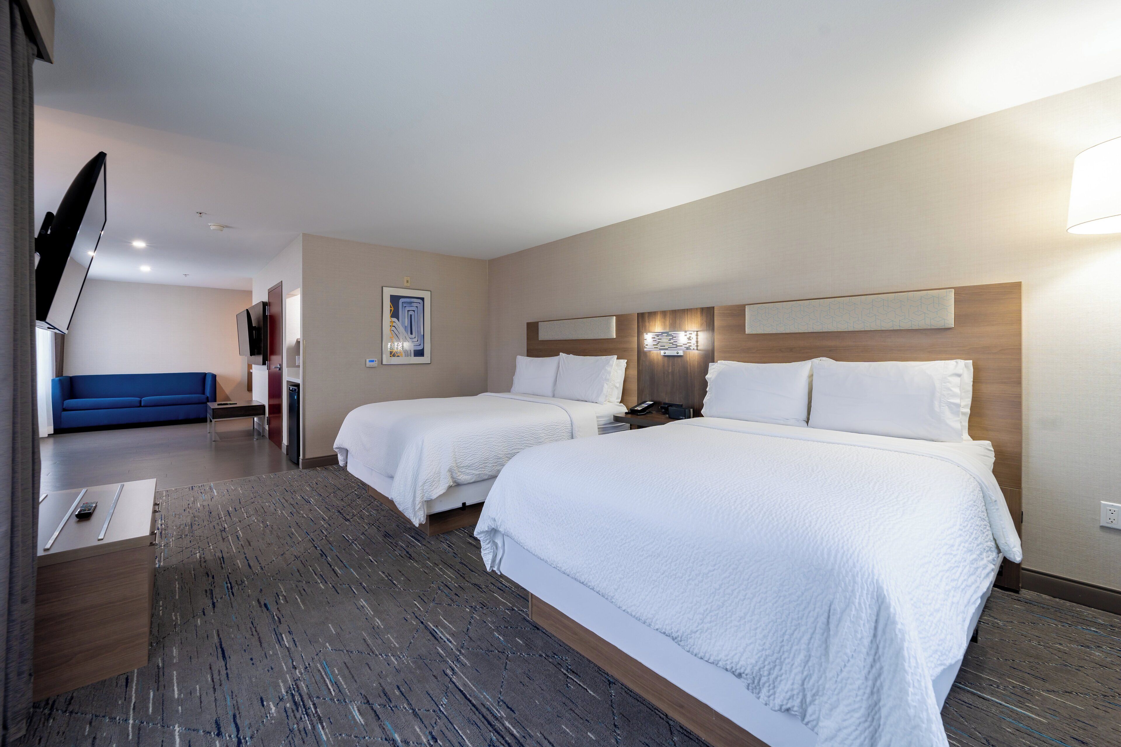 Une chambre d’hôtel avec deux lits, une télévision, un bureau et un canapé bleu.