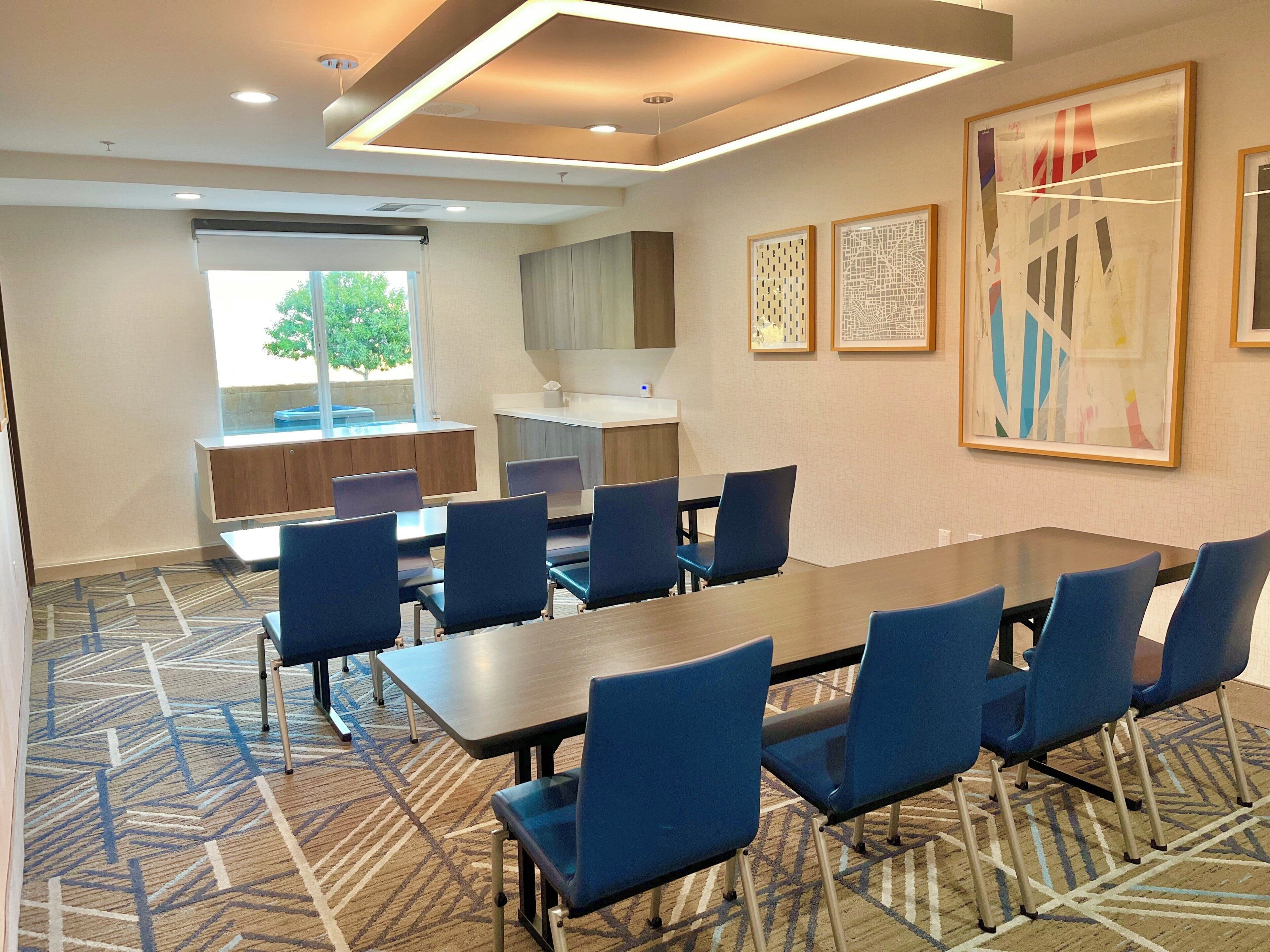 Un salón de conferencias con una mesa larga, sillas azules, alfombra estampada y obras de arte en las paredes.