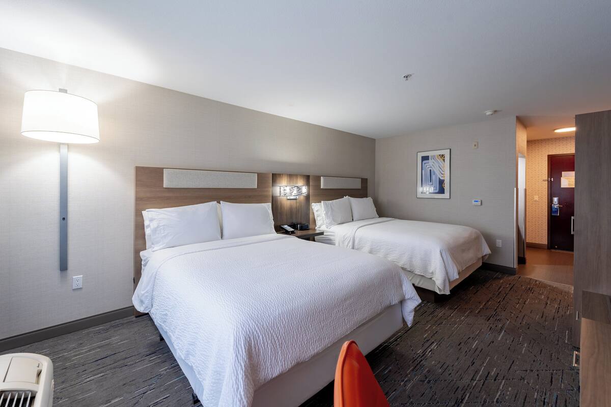 A hotel room with two beds, a nightstand, a lamp, and a painting on the wall.