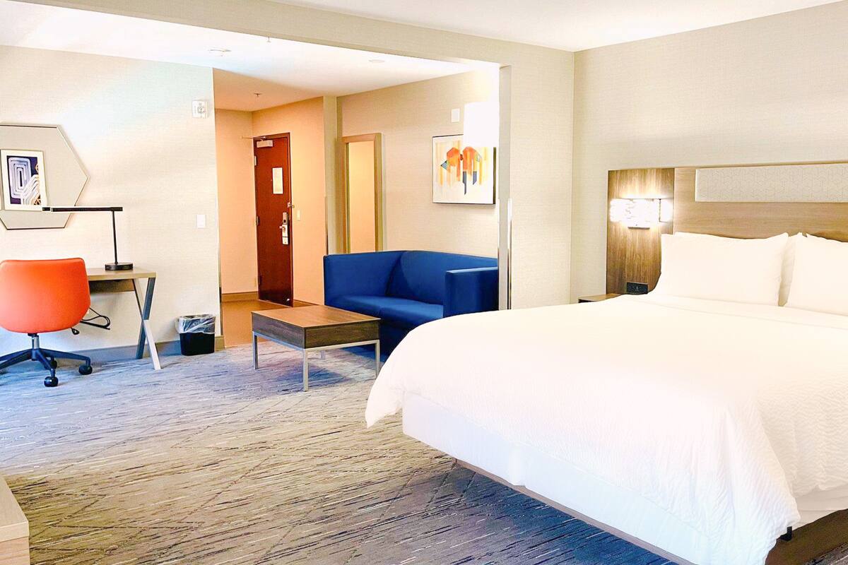 A hotel room with a large bed, a desk with a chair, a blue sofa, and a small table.