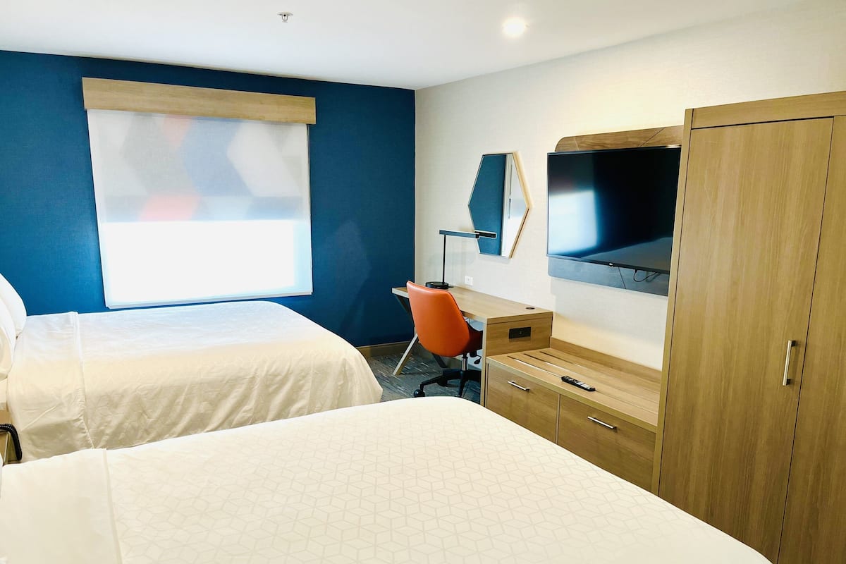 A hotel room with two beds, a desk, a TV, and a wardrobe.
