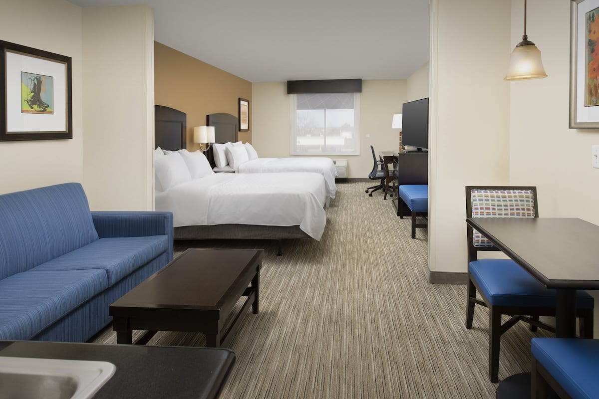 A hotel room with a blue sofa, two single beds, a desk with a chair, and a TV.