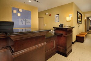 Una recepción de hotel con mostrador de madera, un letrero de Holiday Inn Express, una cámara de seguridad y un certificado enmarcado en la pared.