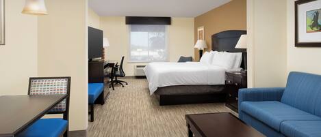 A hotel room with a bed, a desk, a chair, a sofa, and a lamp.