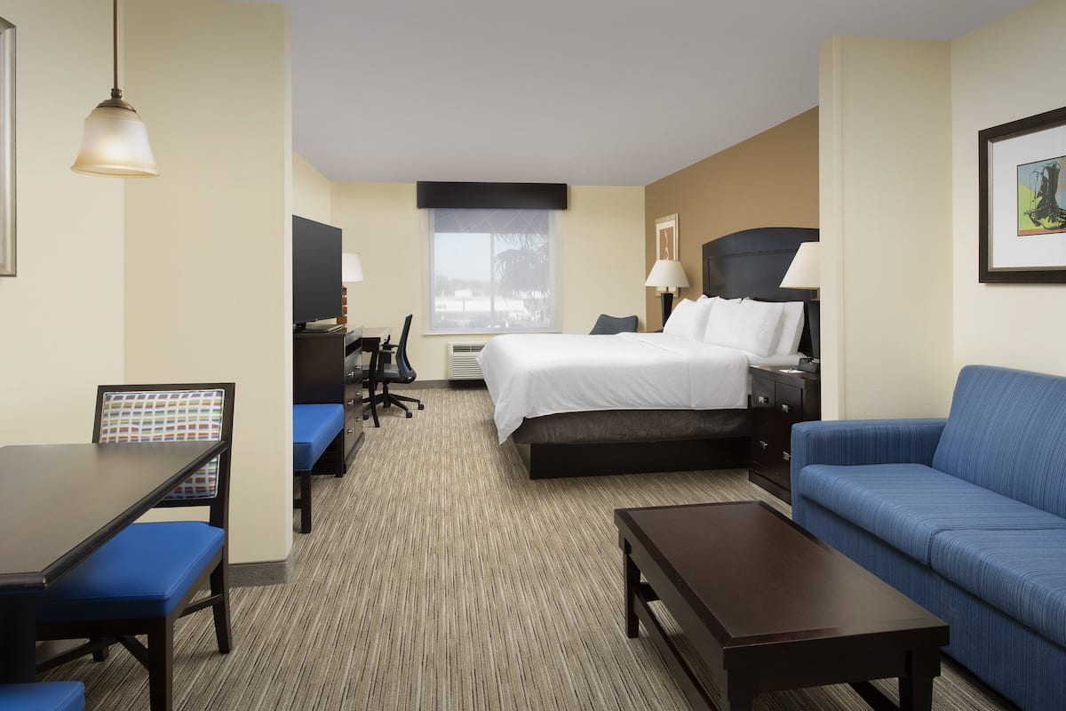 A hotel room with a bed, a sofa, a desk with a chair, and a small table.