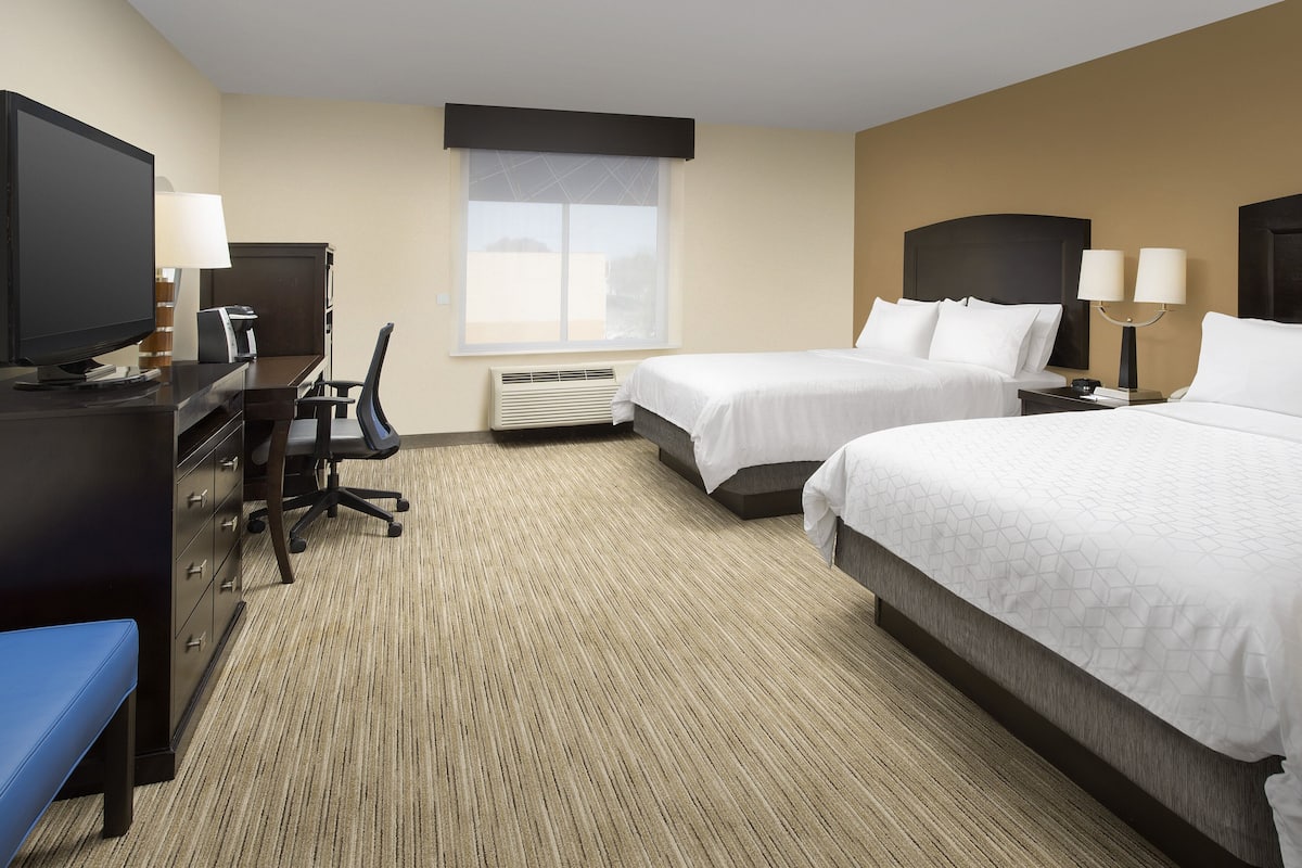 A hotel room with two beds, a desk with a computer, a television, and a window with blinds.