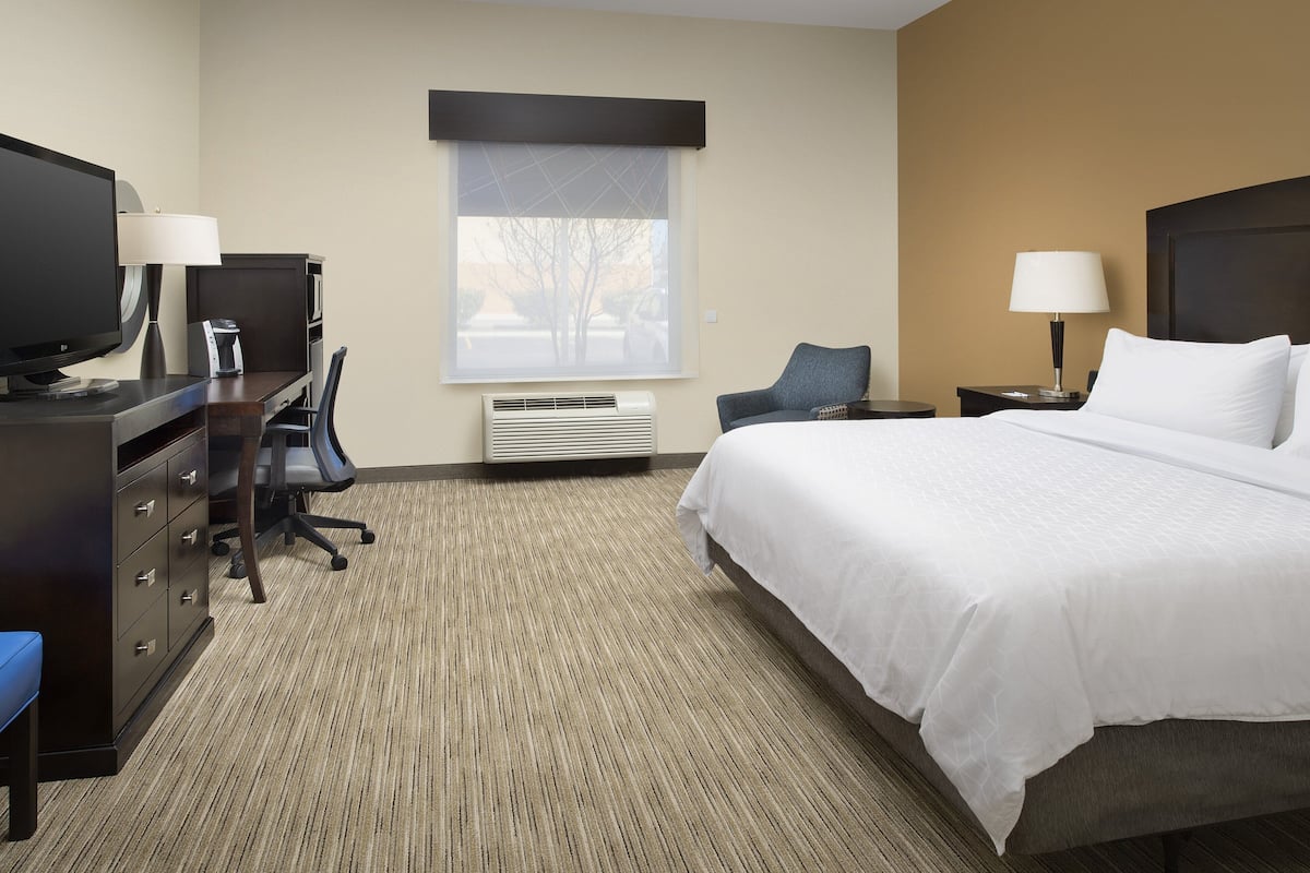 A hotel room with a bed, desk, chair, and a window with blinds.