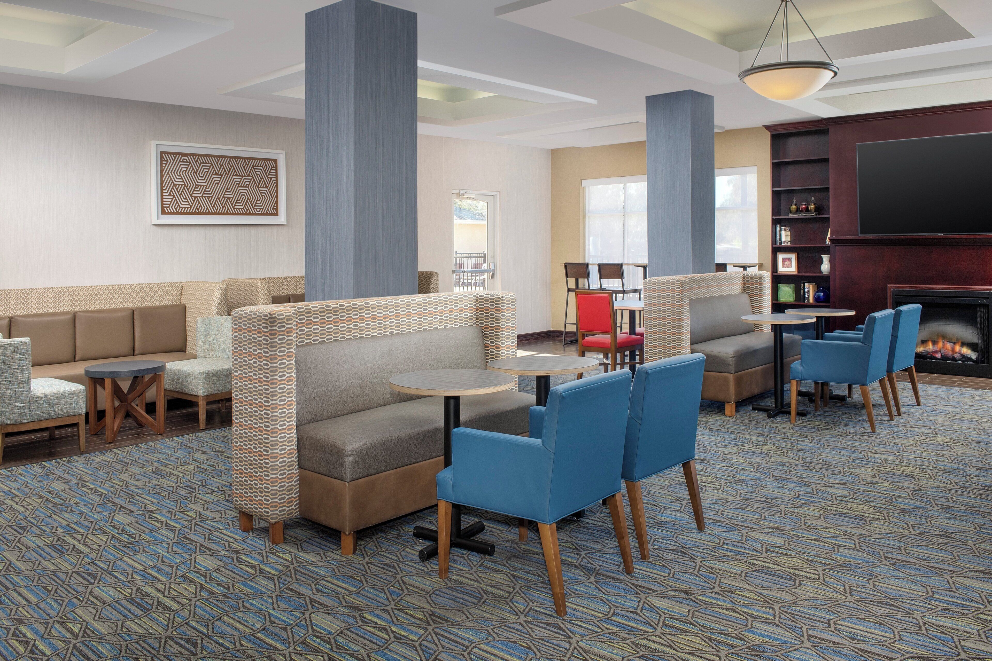 A hotel lobby with seating areas, a fireplace, and a television.