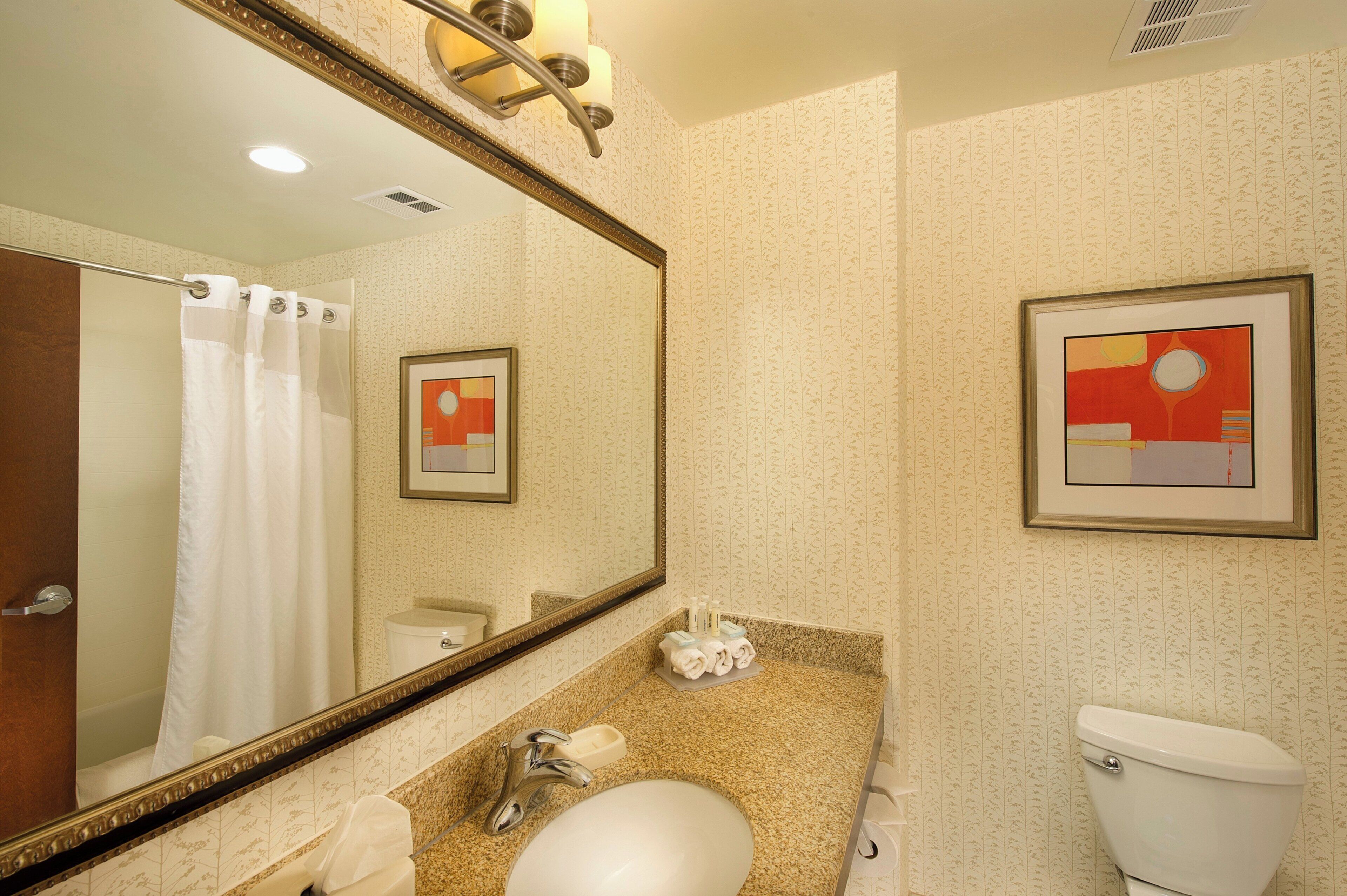 A bathroom with a large mirror, a sink, a toilet, and a framed abstract painting on the wall.