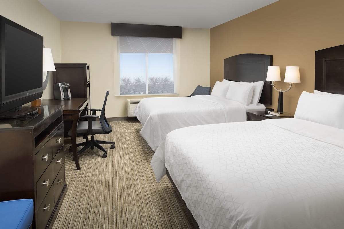 A hotel room with two beds, a desk with a television, a chair, and a window with a view.