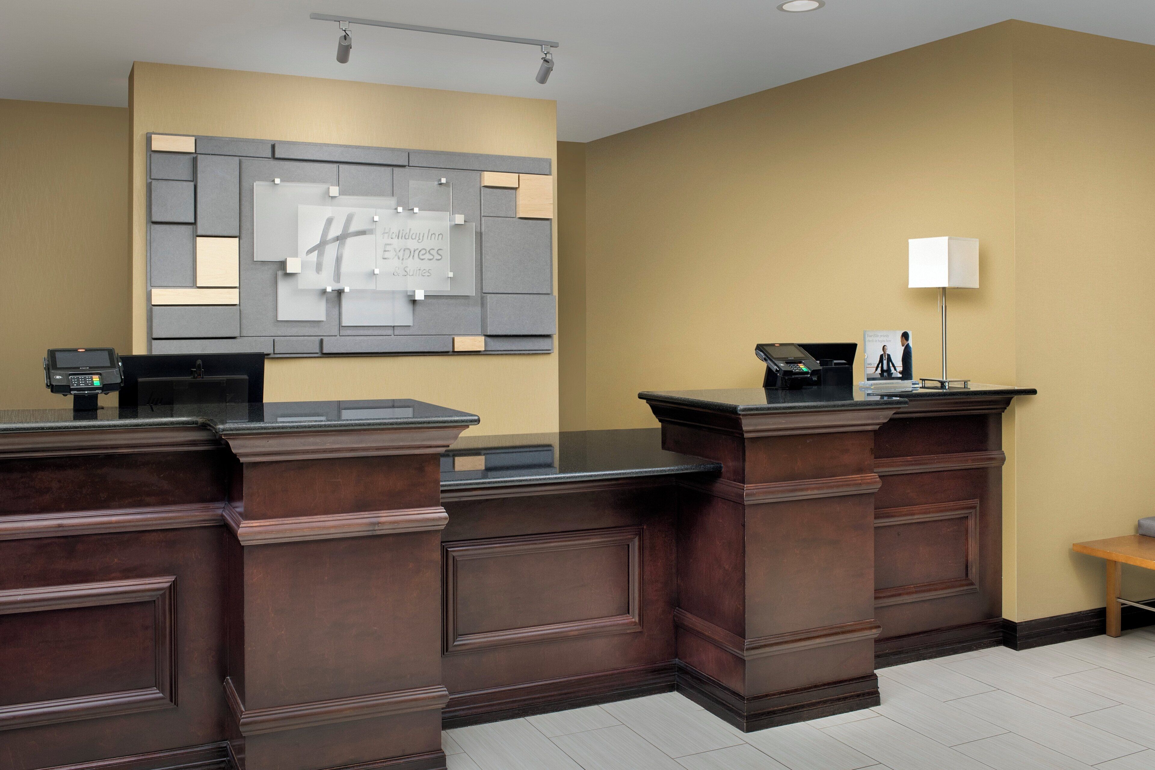 A reception desk with a digital kiosk, a wall-mounted information board, and a desk lamp.
