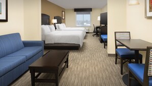 A hotel room with a blue sofa, two single beds, a desk with a chair, and a view of the city through the window. - Holiday Inn Express Hotel & Suites Uvalde by IHG (Uvalde)