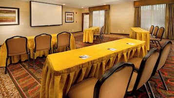 A conference room with a long table, multiple chairs, a projector screen, and a carpeted floor.