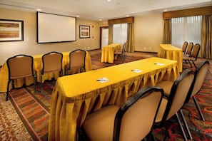 A conference room with a long table, multiple chairs, a projector screen, and a carpeted floor.