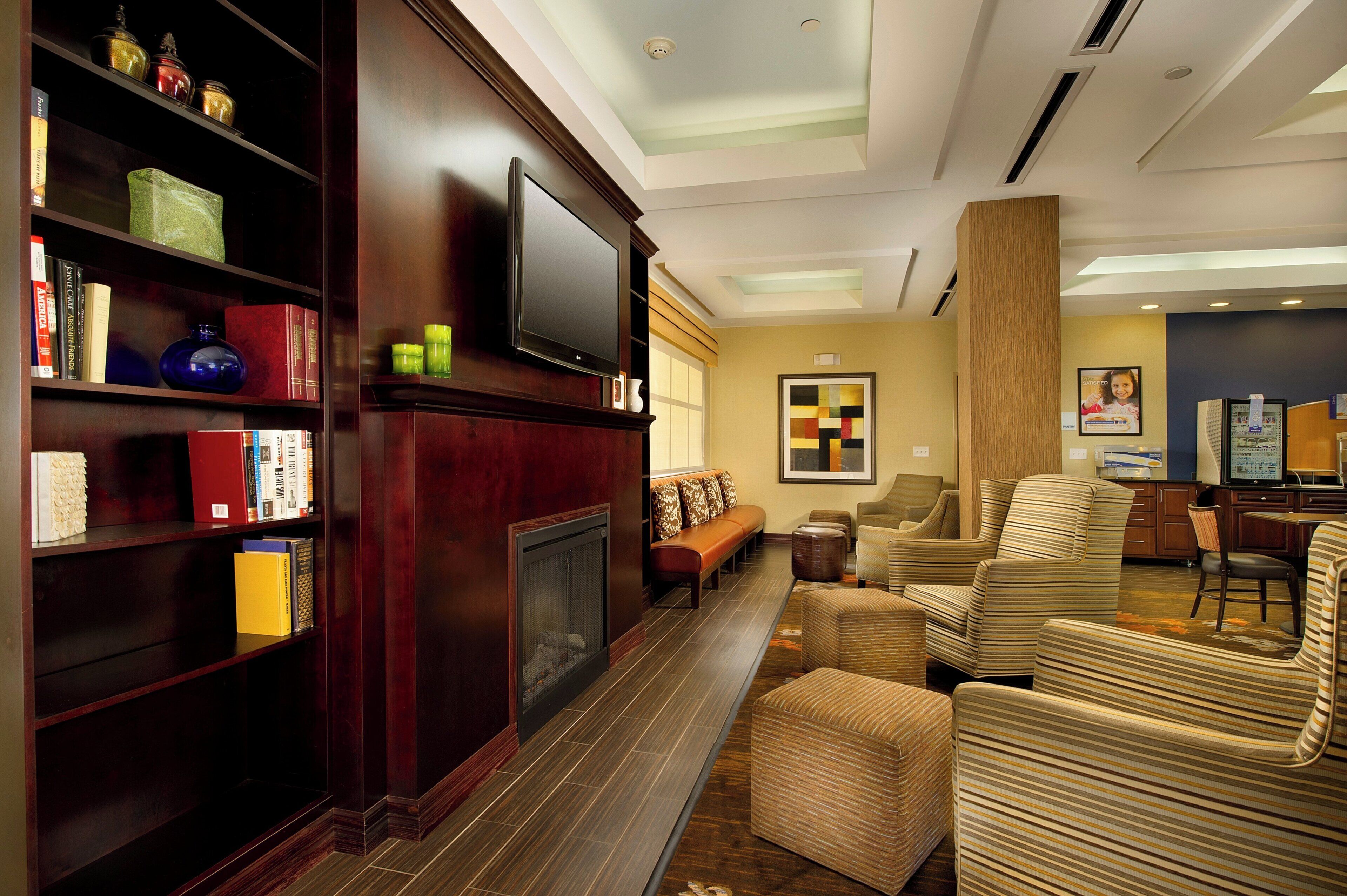 A hotel lobby with a fireplace, bookshelves, a television, and seating area.