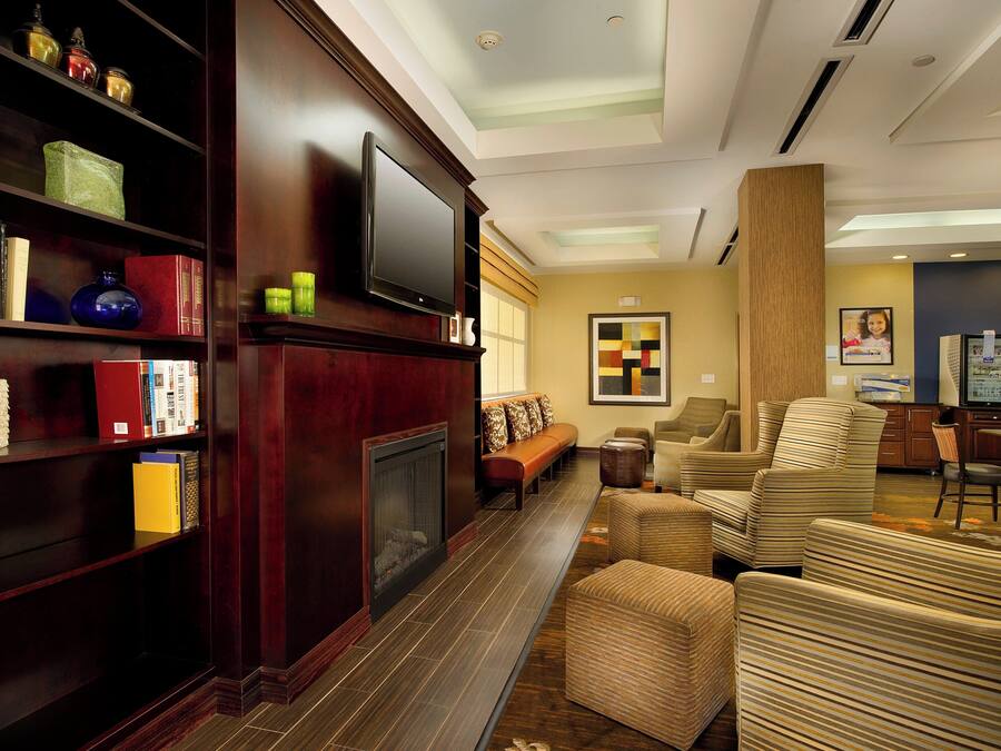 A hotel lobby with a fireplace, bookshelves, a television, and seating area.