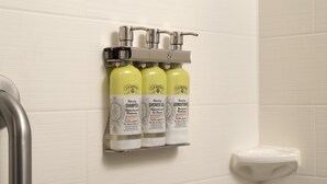 A bathroom with a wall-mounted shelf holding three bottles of J.R. Watkins products: shampoo, shower gel, and conditioner. - Holiday Inn Express Hotel & Suites Uvalde by IHG (Uvalde)