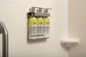 Een badkamer met een wandplank waarop drie flessen J.R. Watkins producten staan: shampoo, douchegel en conditioner.