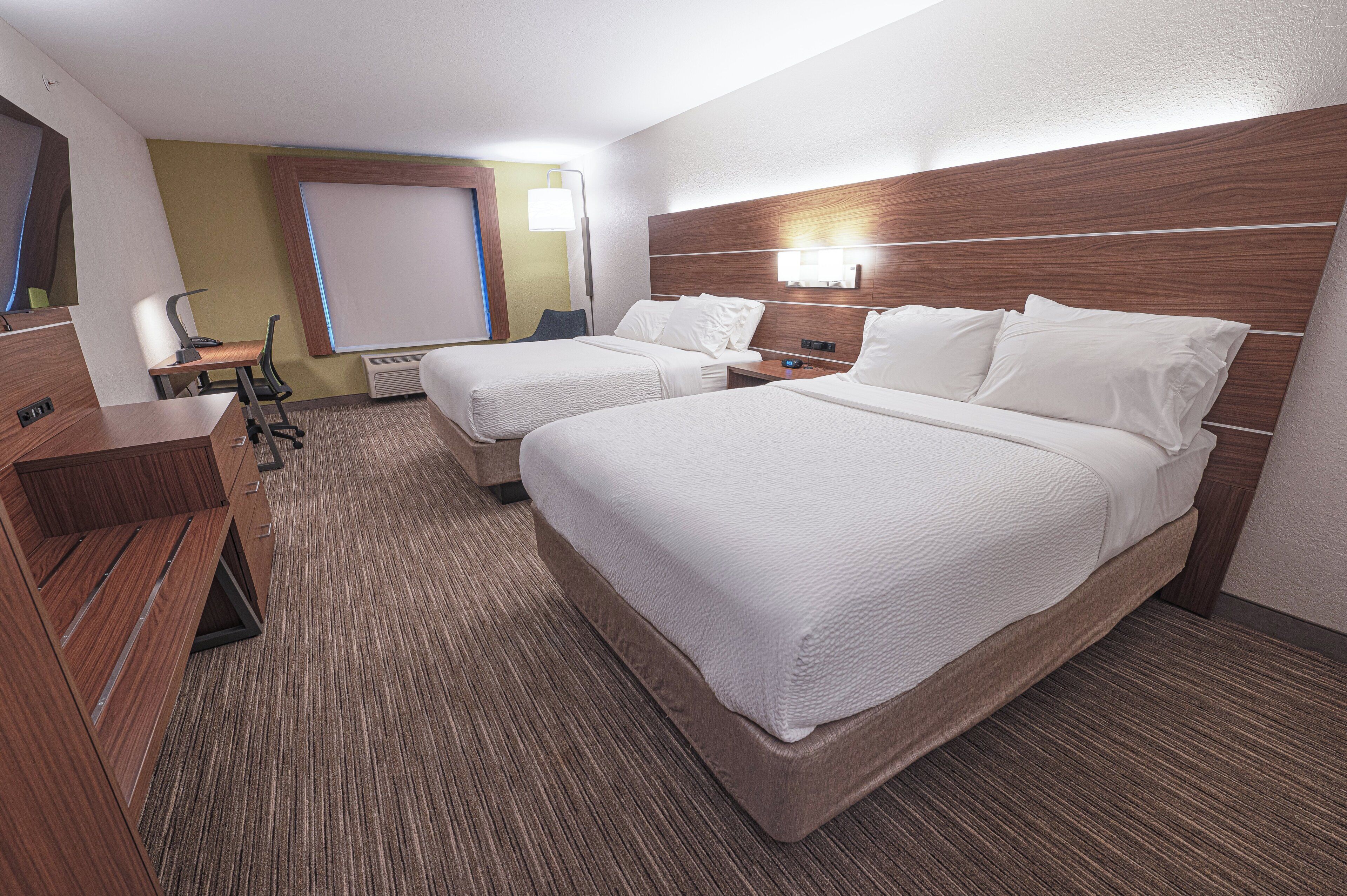 A hotel room with two beds, a desk, a chair, and a large mirror.