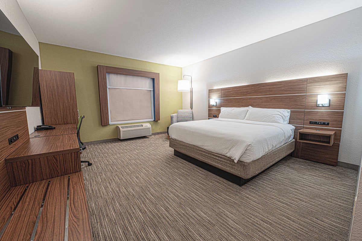 A hotel room with a bed, a desk, a chair, a lamp, and a window.