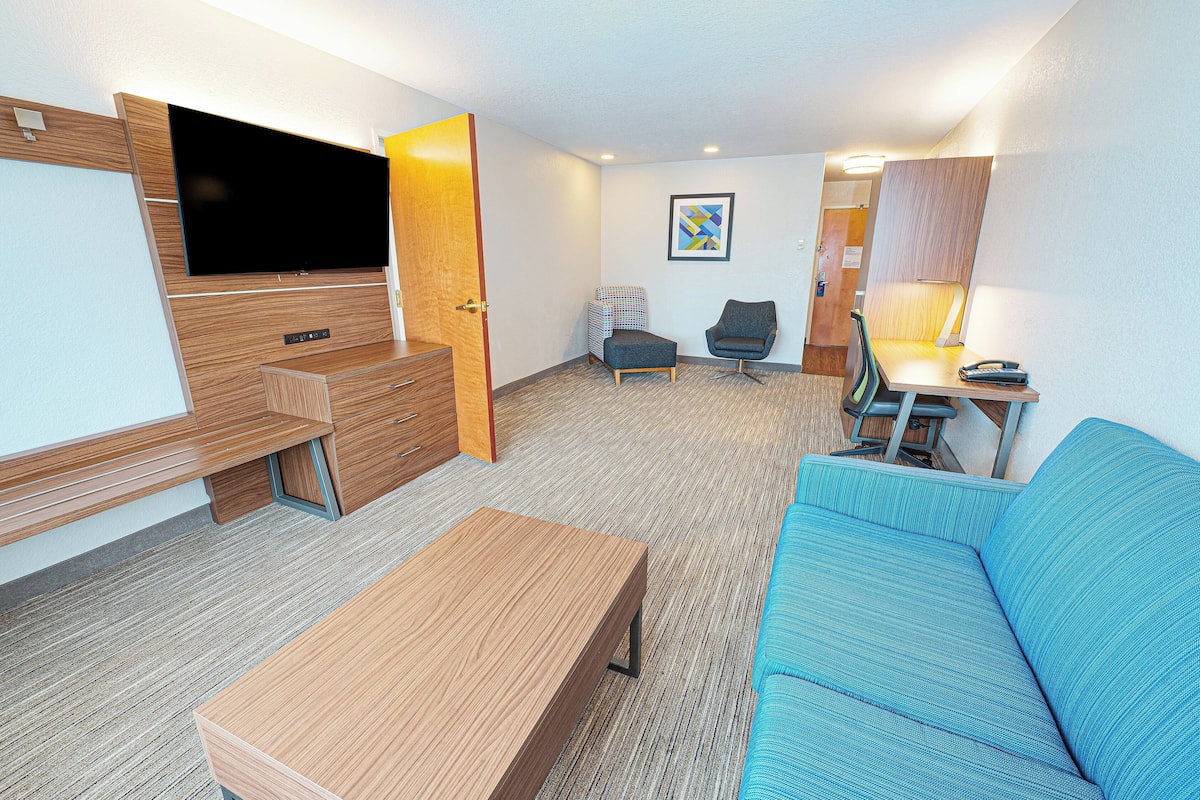 A compact hotel room with a sofa, a small table, a TV, a desk, and a chair.