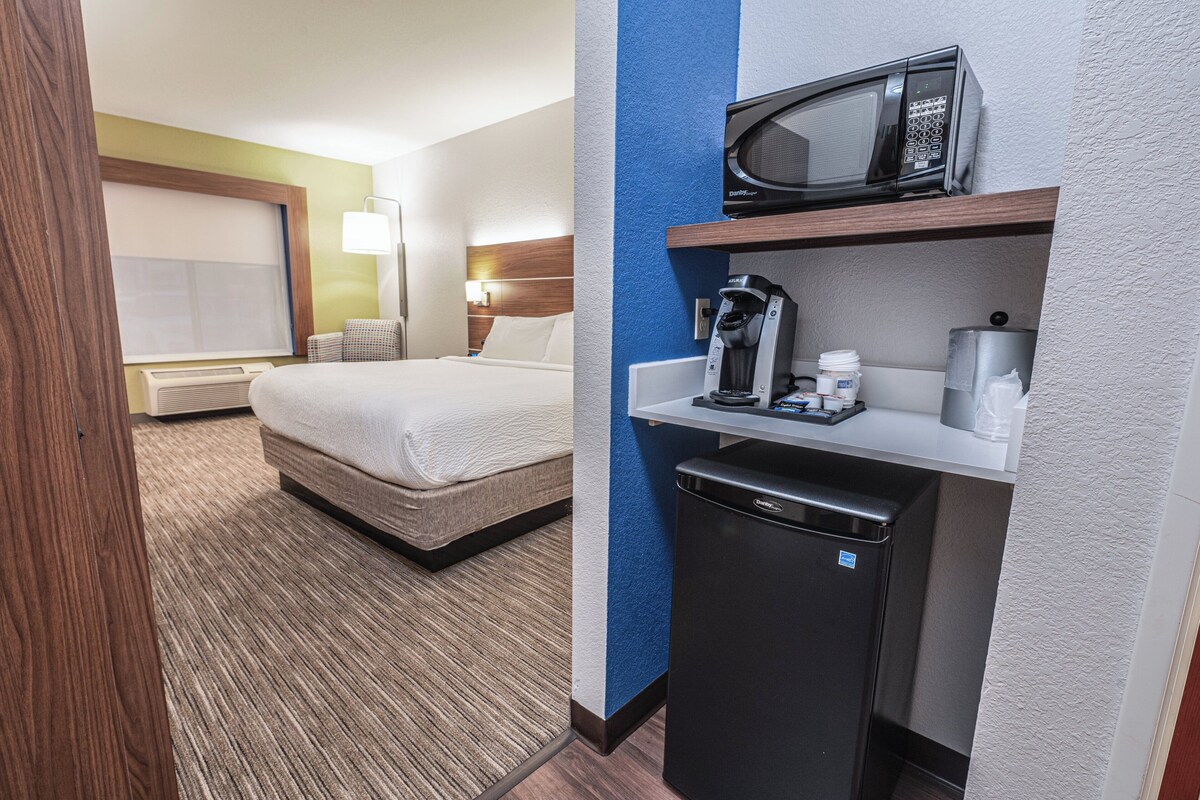 A hotel room with a bed, a coffee machine, a microwave, and a small refrigerator.