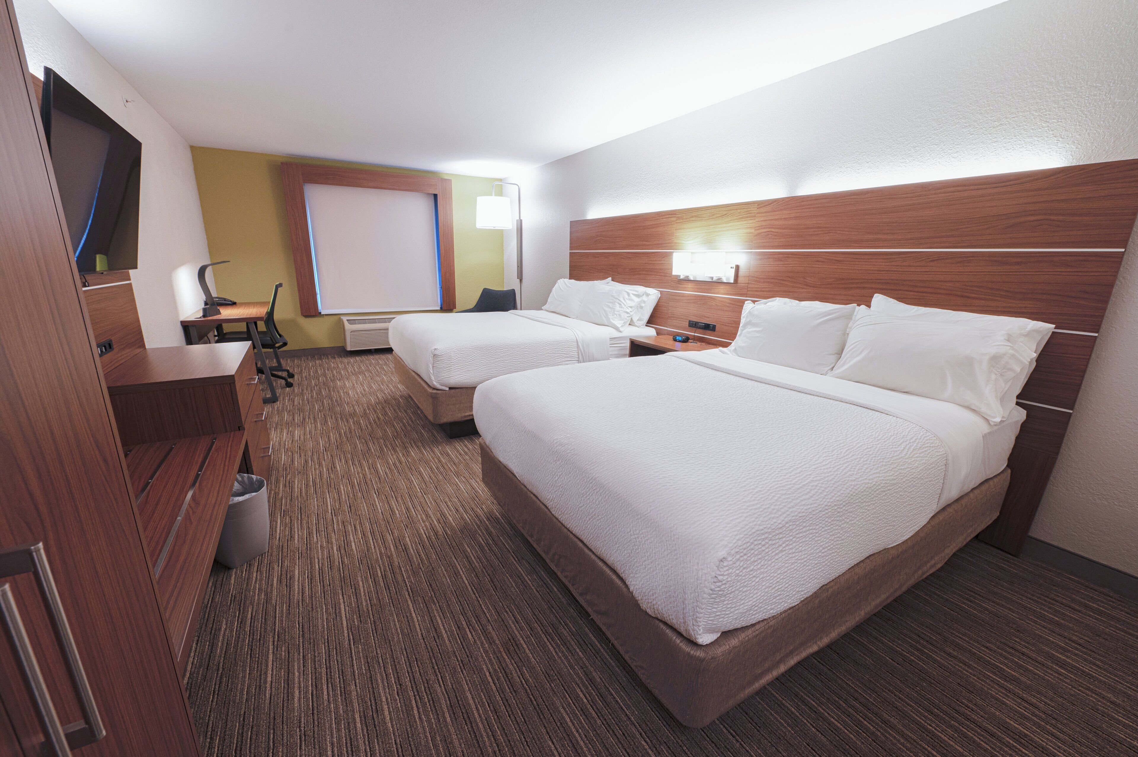 Habitación de hotel con dos camas, un escritorio, una silla, un televisor y una ventana con persianas.